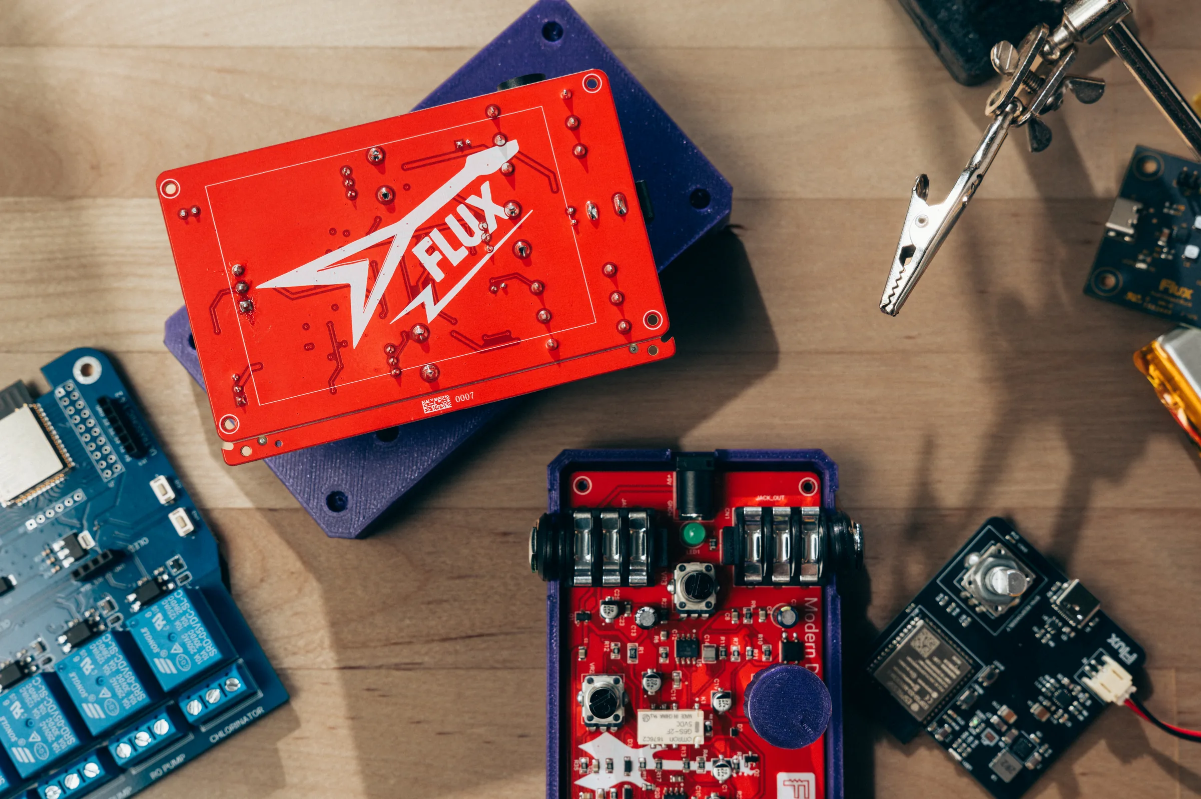 A guitar pedal board in a purple enclosure, next to a red board with the Flux logo