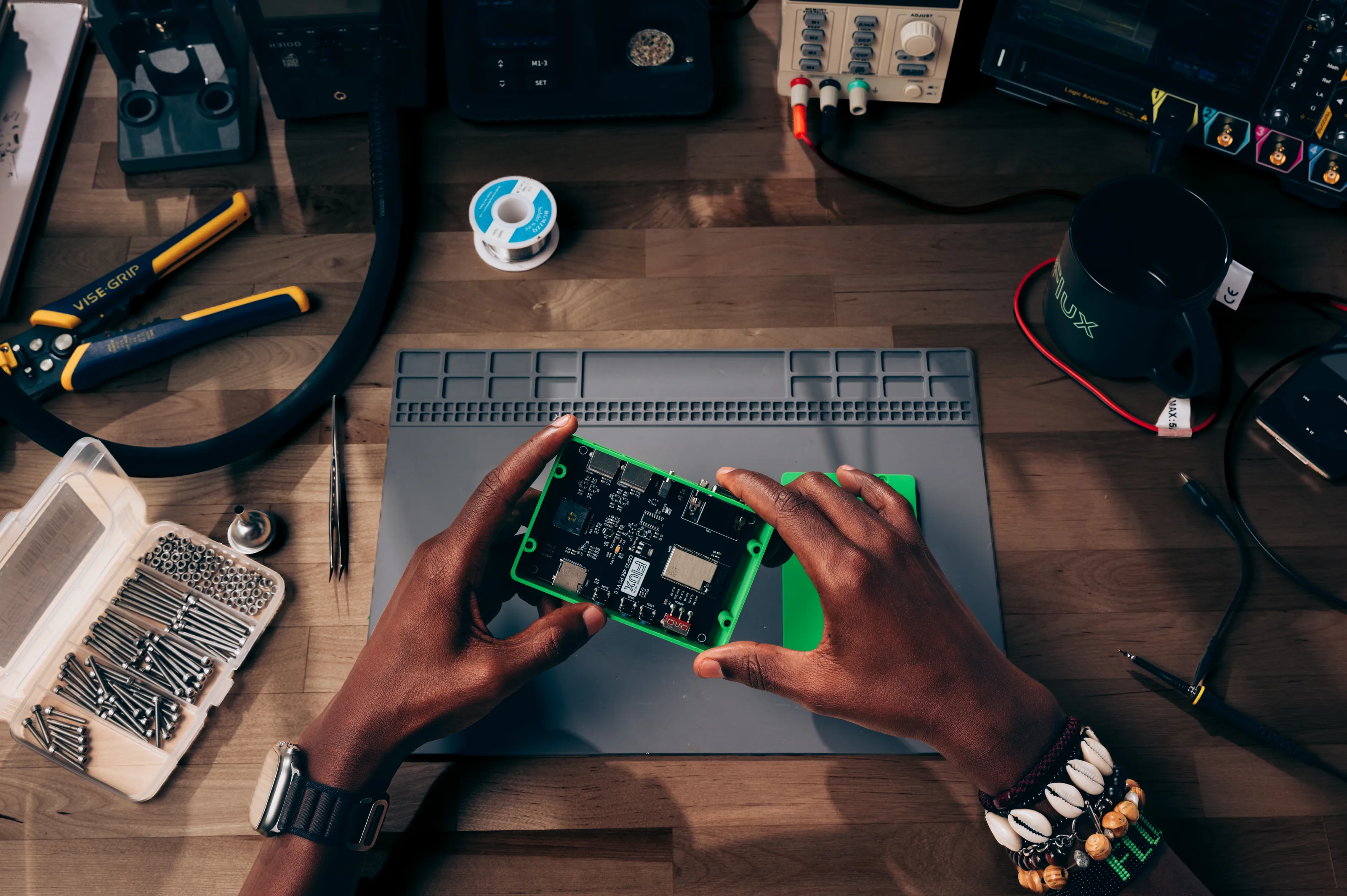 Engineer holding a green Flux-designed circuit board over a workbench