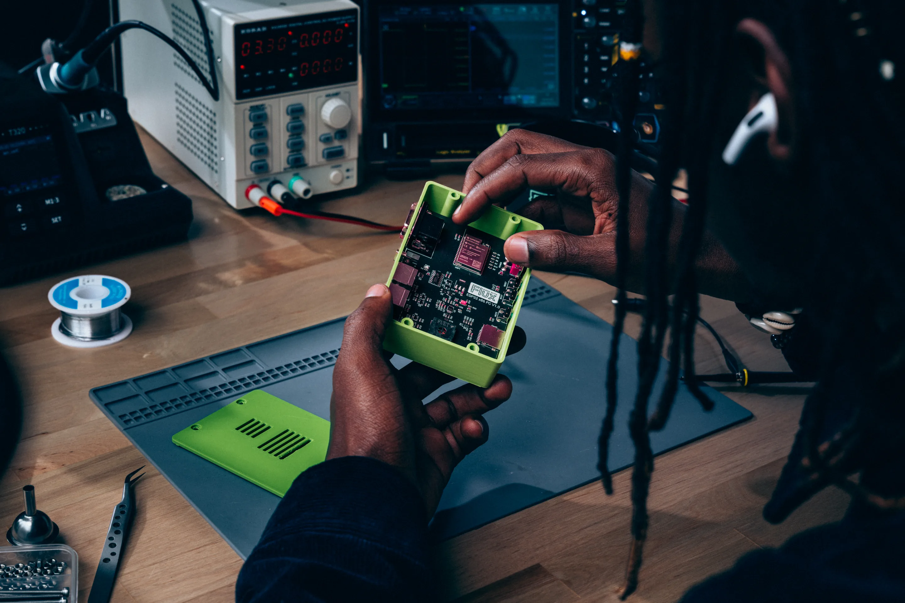 An engineer inspecting a circuit board inside a green enclosure at an electronics workbench